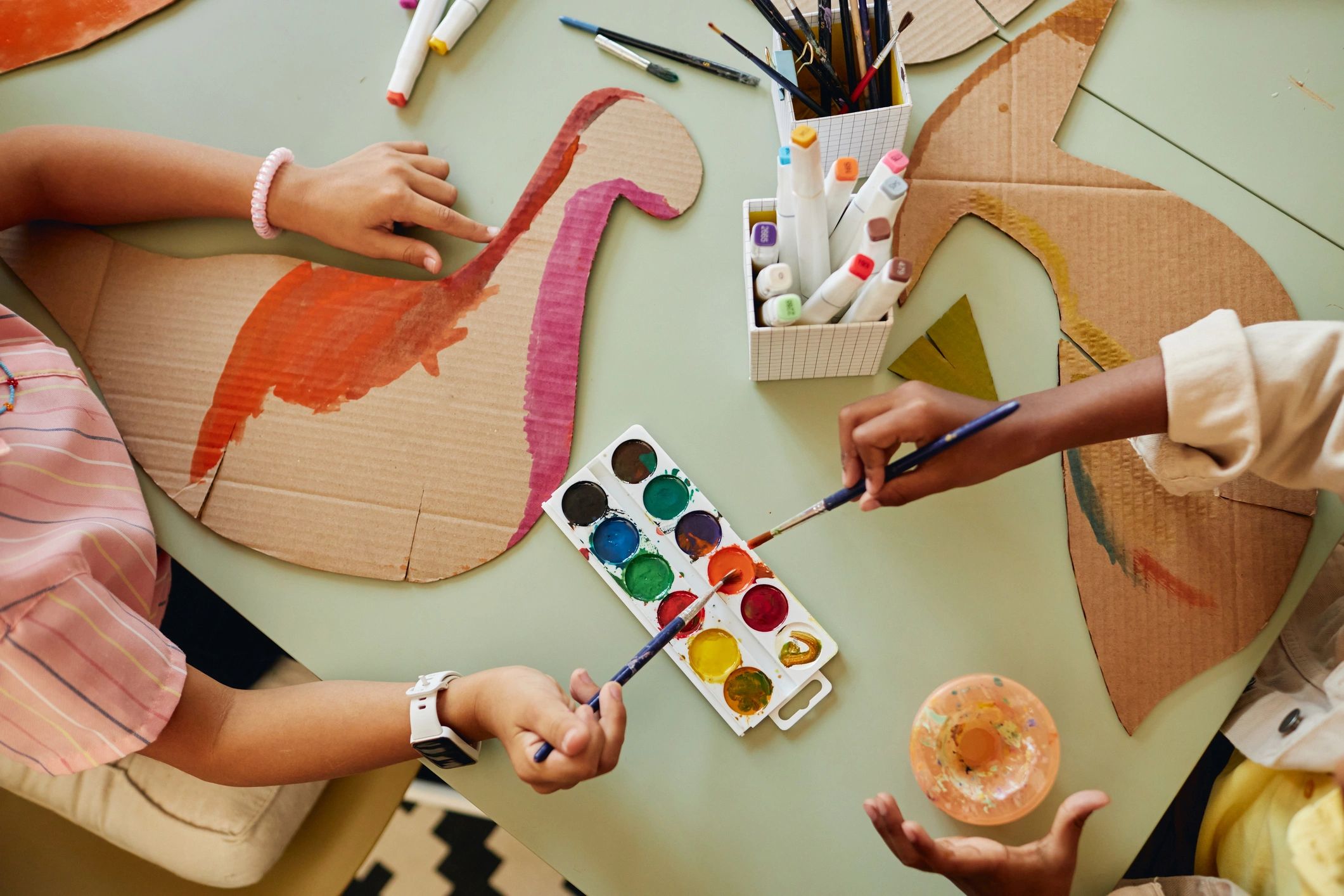 Top-down view of kids painting cardboard dinosaur crafts