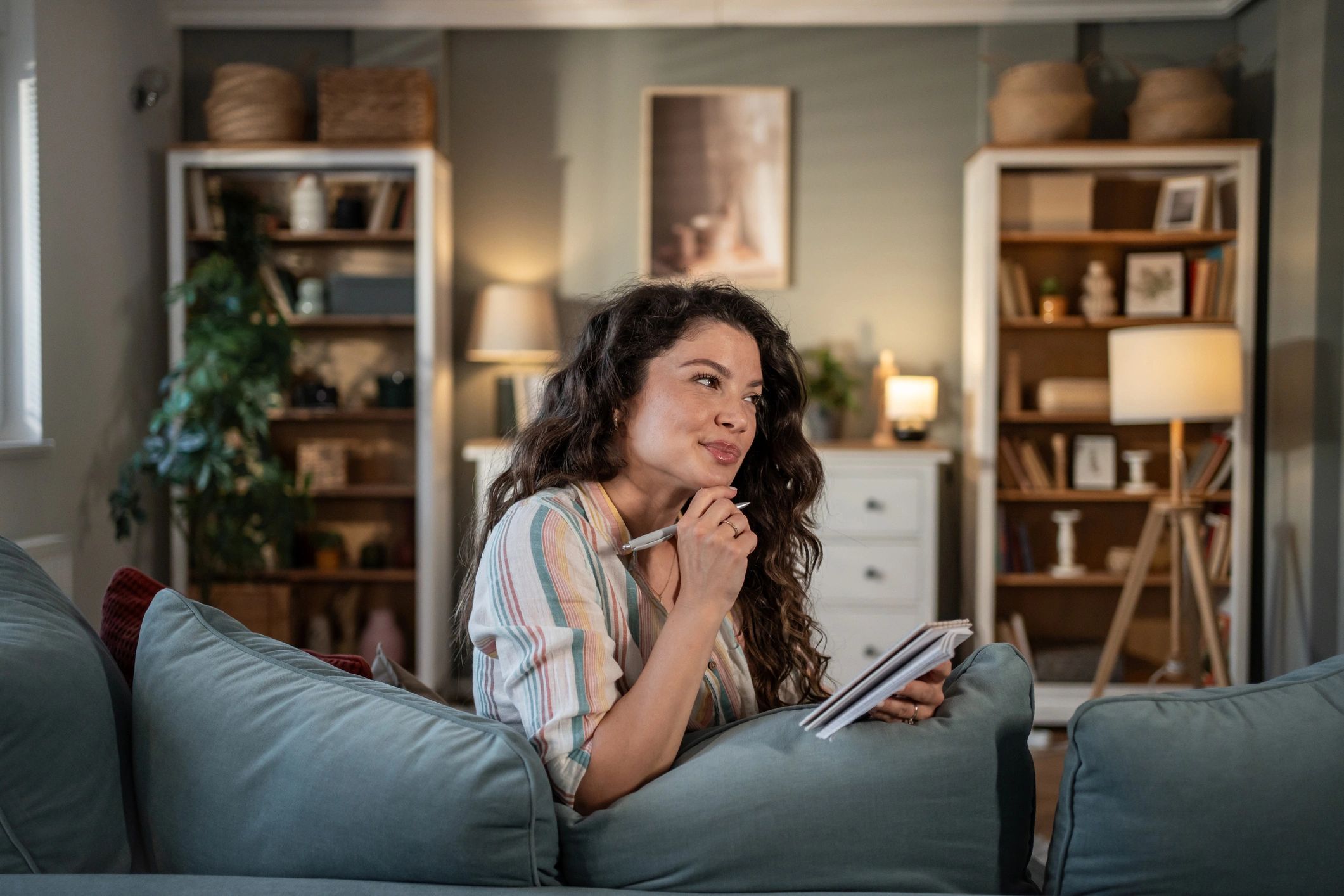 Woman writing notes in a notebook on a sofa at home